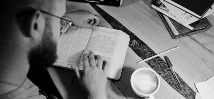 Grayscale photo of a person reading a bible