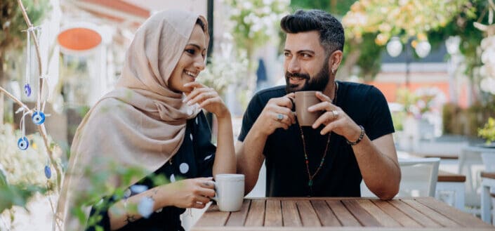 Man and woman in headscarf drinking from cups outside