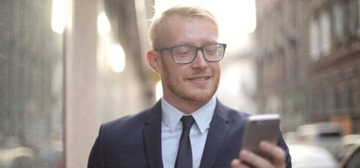 Smiling male entrepreneur in eyeglasses browsing smartphone in downtown