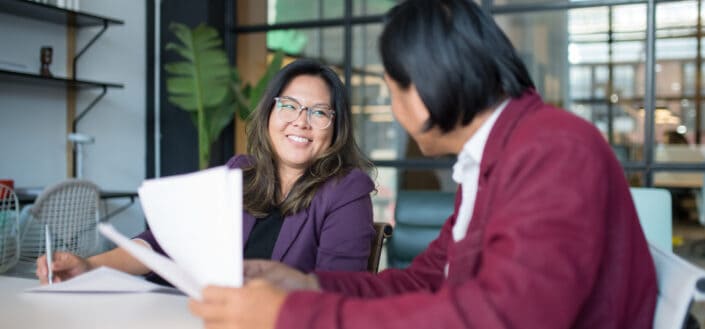 Woman in purple blazer smiling while holding a pen