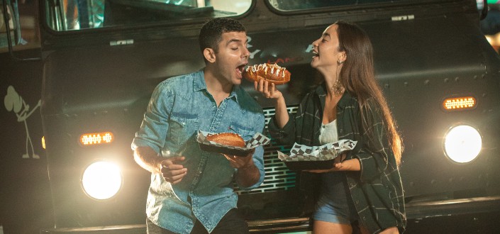 A couple eating a bread in front of a jeep