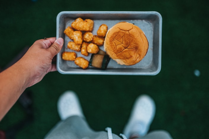 A man holding a plate with tater tots and burger