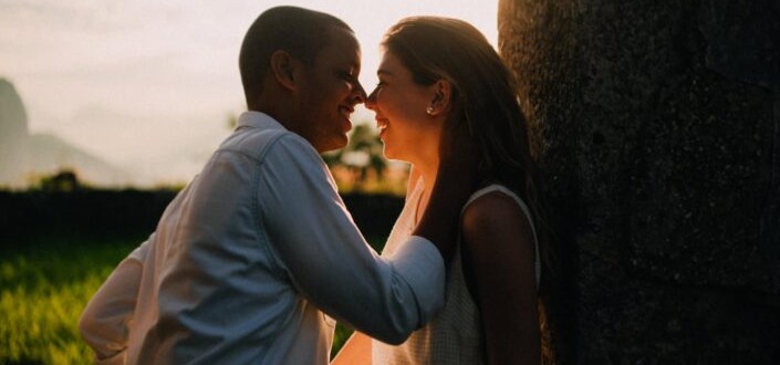 Romantic man and woman smiling while face to face under the sunset