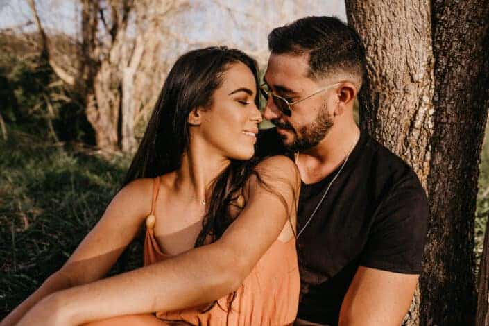 Couple about to kiss near a tree.