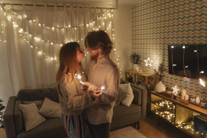 A man and a woman looking at each other while holding a burning sparkler at home
