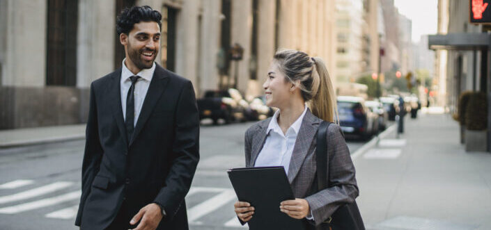 businessman-and-businesswoman-talking-and-smiling-while-crossing-the-street-stockpack-pexels