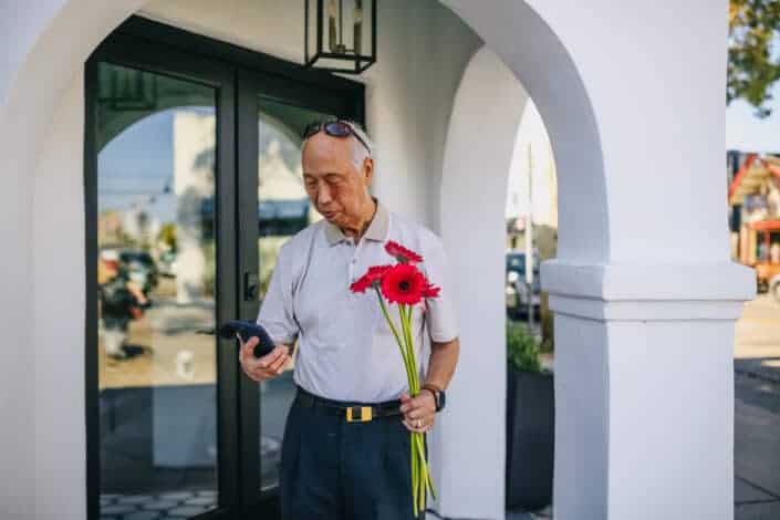 Old man holding red flowers and texting on his smartphone