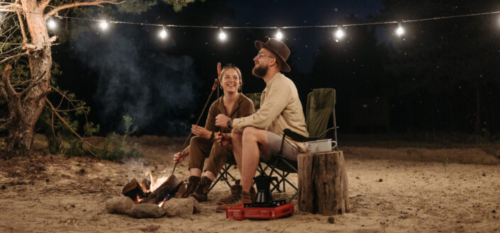 A Couple Sitting on Chair While Grilling on Campfire