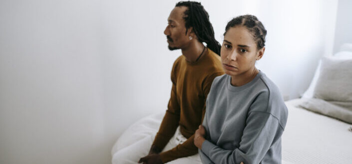 Unhappy black couple sitting on bed together