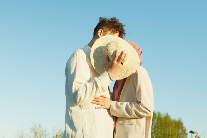 A Couple Kissing Each Other behind a hat