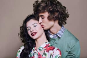 Portrait of Young Couple Kissing Against Gray Background