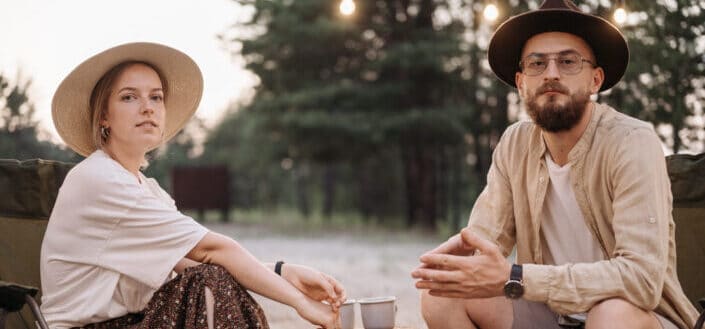 Man and a woman wearing casual clothes sitting on a park drinking some coffee