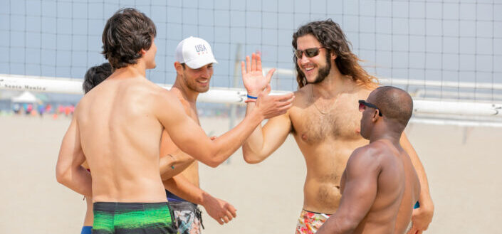 five guys playing beach volleyball under the heat of the sun