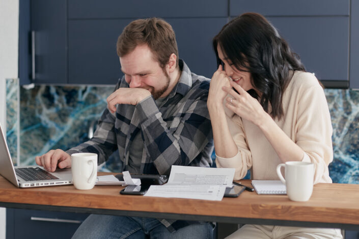 smiling man and woman while looking at a laptop screen