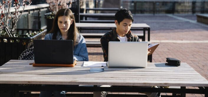 Two youngsters sitting on the park busy working with their laptops