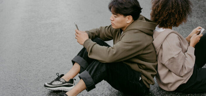 Man and Woman Sitting on the Road While on Their Mobile Phones