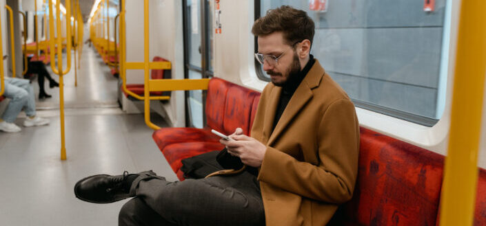 A Man in Brown Jacket Sitting on a Train Seat Holding a Cellphone
