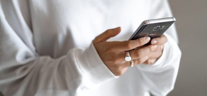 A Person Holding a Phone and Wearing a White Jumper