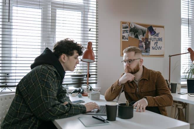 Two Guys Seriously Discussing Something Over a Laptop - Hot Seat Questions