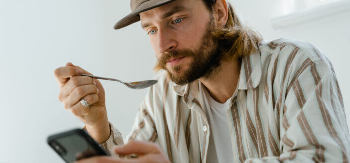 Man Eating While Browsing on His Phone