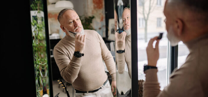 Old man looking in mirror brushing beard