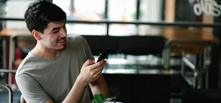 Smiling Man Browsing Smartphone in Cafe
