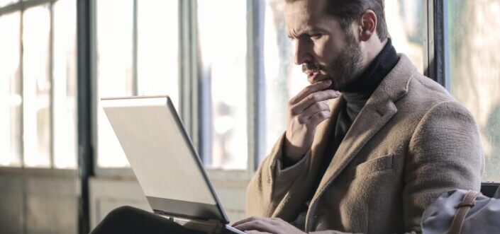 man in brown suit jacket working on his laptop