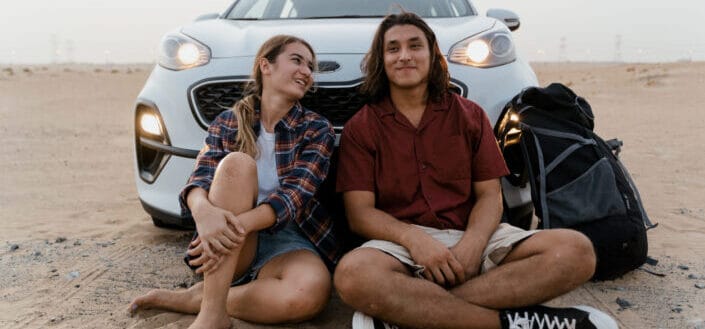 A couple sitting in front of their parked car on a desert