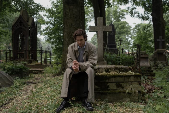 A man in a trench coat sitting on a grave