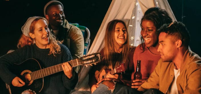 Group of friends singing while sitting on beach shore