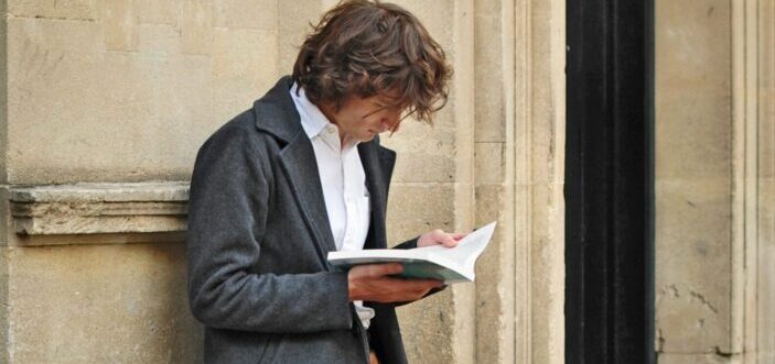 A man is leaning on the wall while reading