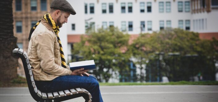man reading a book while sitting on a bench