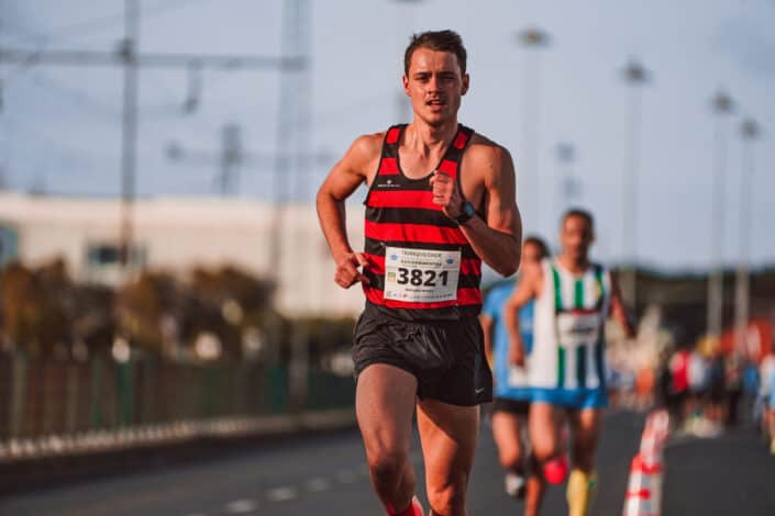 Man in black and red striped tank top running on road