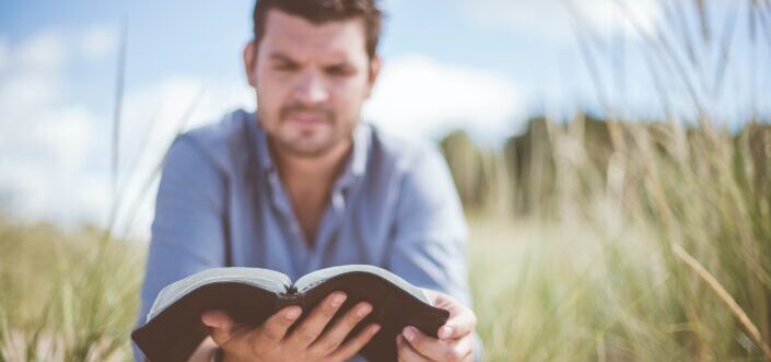 man reading book in grass field