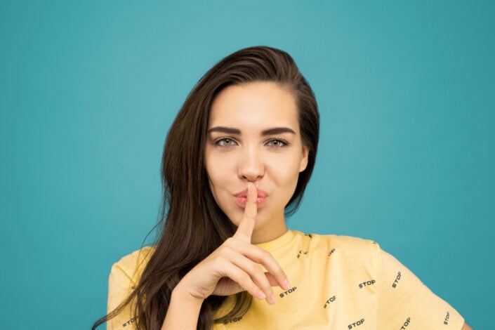 Woman Doing the Shh Sign While Standing in Front of Blue Background