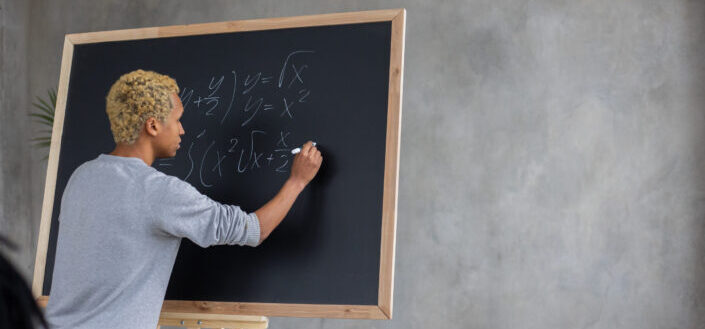 Serious black student writing mathematical example on blackboard
