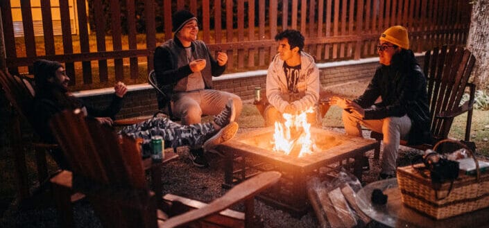 Smiling friends speaking against bright flame in camp at night