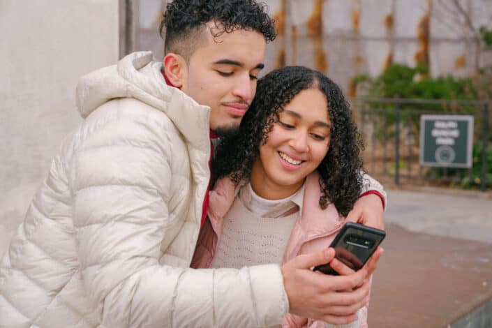 Smiling couple hugging and using smartphone on street