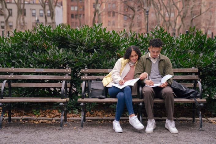 couple preparing homework on bench in city park