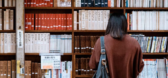 Woman wearing brown shirt carrying black leather bag on front of library books