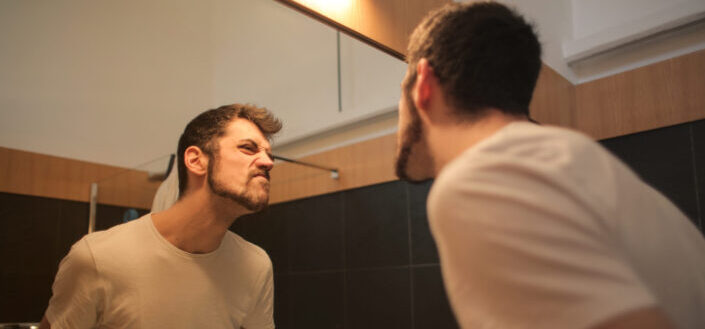 Young unshaven man looking at his face in the mirror