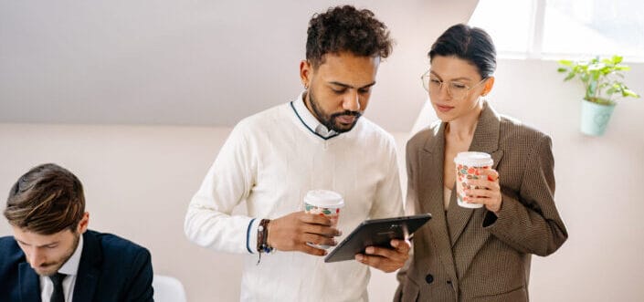 A man and woman looking at the tablet while holding a cup of coffee