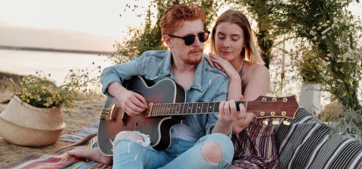 A man in denim jacket playing guitar beside a woman