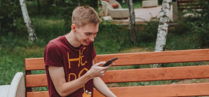 A man sitting on a wooden bench using his mobile phone