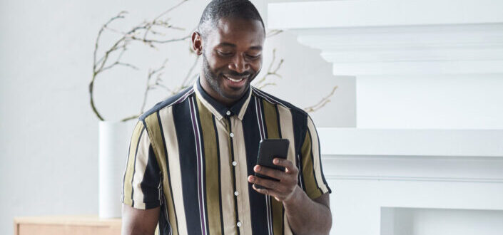 A man wearing a checkered dress shirt using his smartphone while leaning on a chair