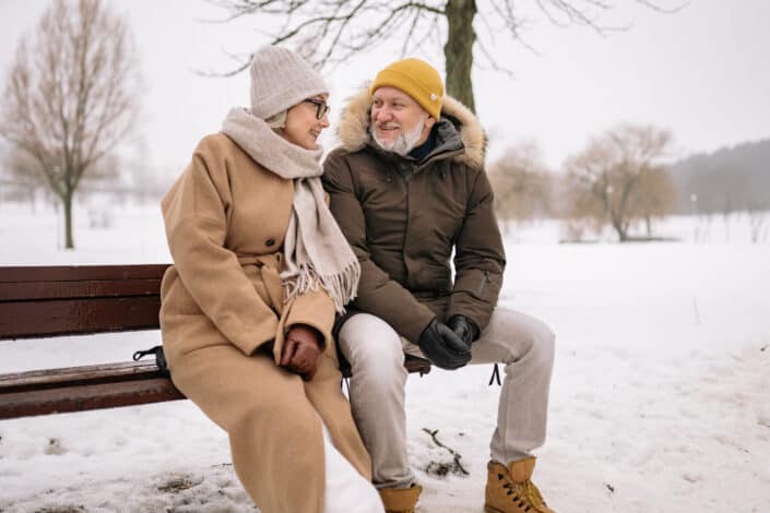 An elderly couple sitting on the park bench in winter