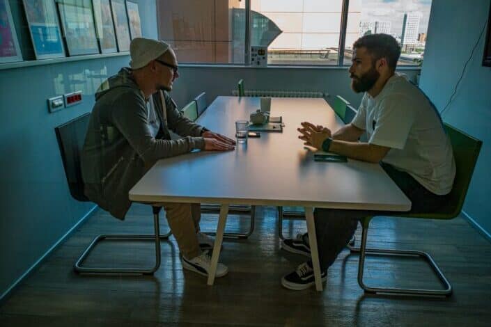 Two guys sitting across each other on a table talking about something serious