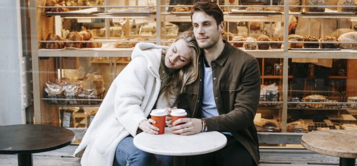 Young couple bonding while sitting near bakery with hot drinks
