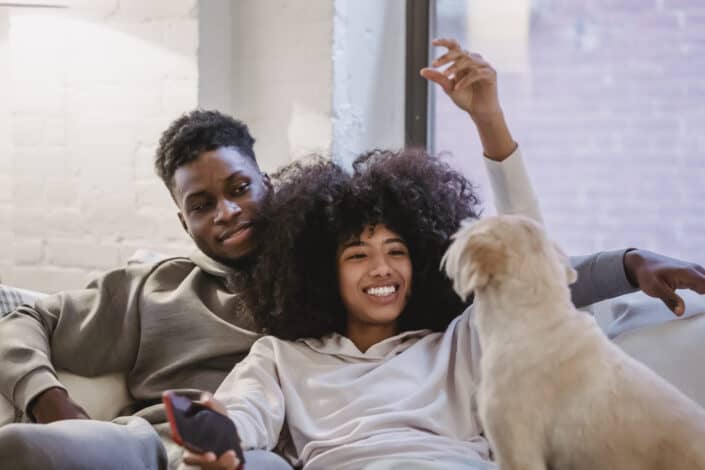 Cheerful black girlfriend playing with obedient dog near boyfriend