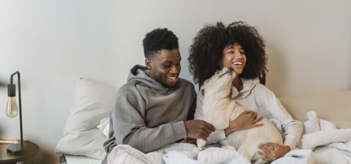 couple hugging cute dog while on bed